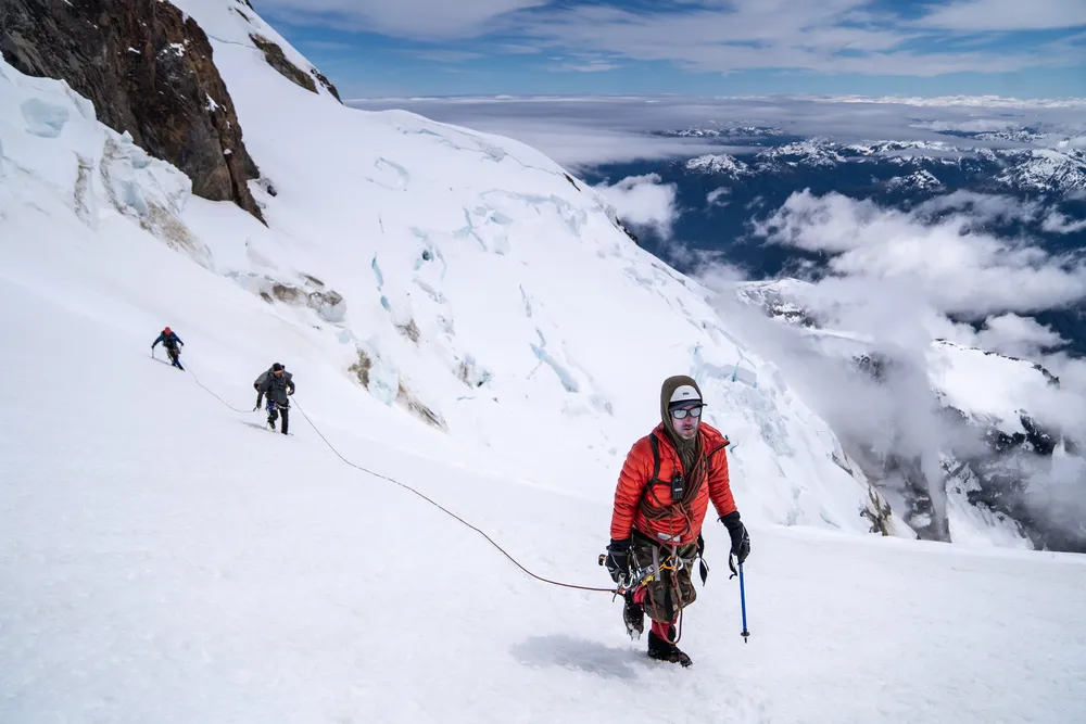 Fotografía de un hombre con chamarra roja, gorro y lentes escalando la cima del volcán Calbuco en Chile.