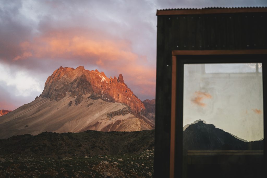 Fotografía a lo lejos de una montaña con el cielo rosa y azul donde hay refugios para turistas en Chile.