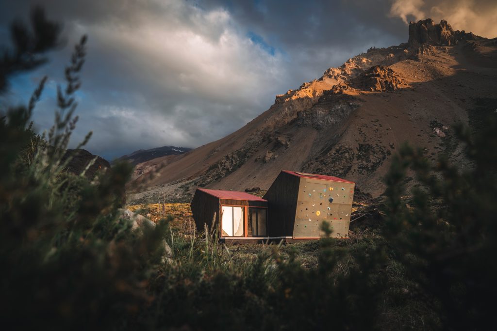 Fotografía de una estructura hecha de madera con ventana y techo rojo que funciona como refugio de montaña.