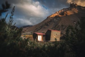 Fotografía de una estructura hecha de madera con ventana y techo rojo que funciona como refugio de montaña.