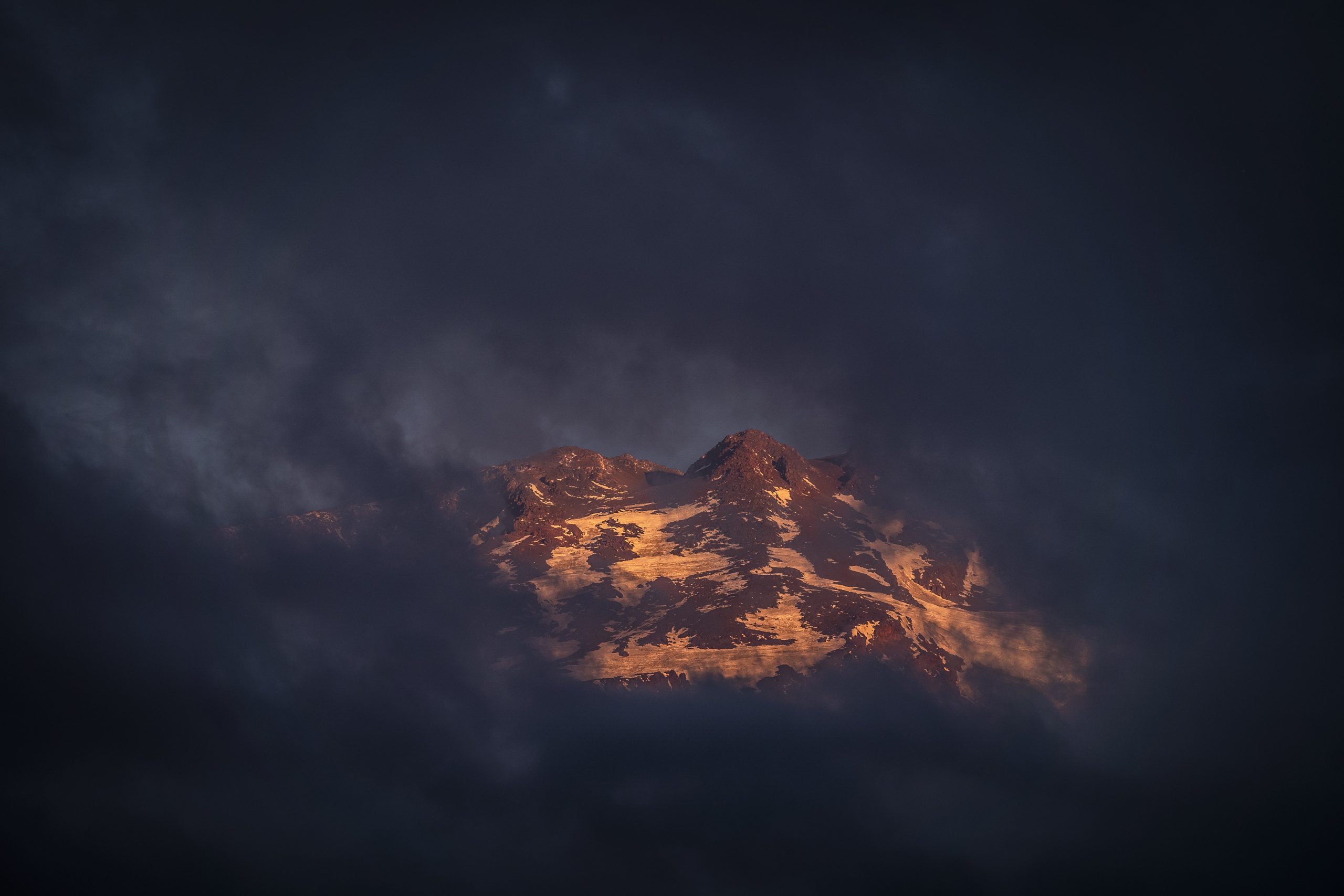 Fotografía a distancia de una cordillera rodeada por nubes azules, lugar donde hay que tener cultura de montaña.